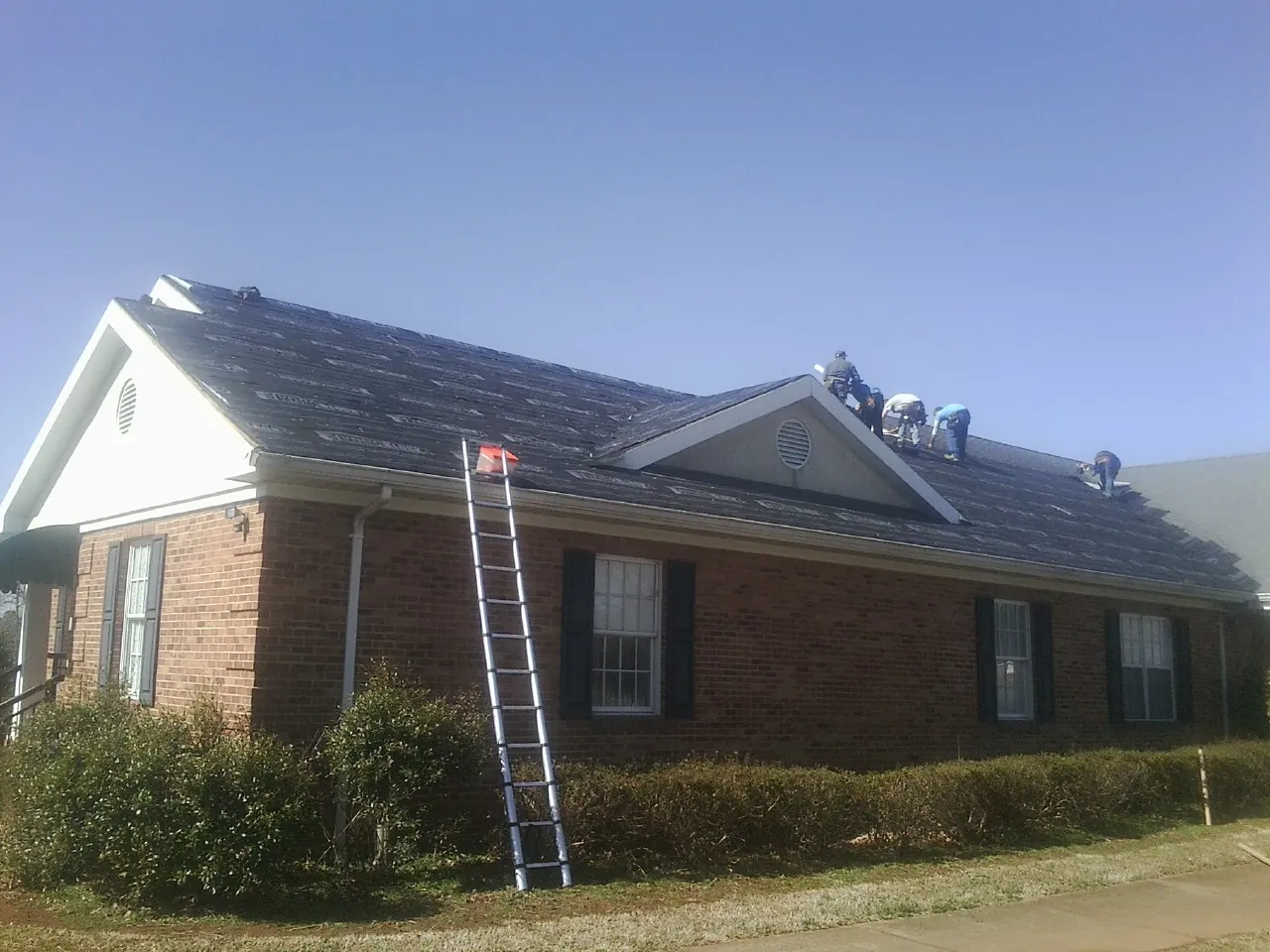 Crew tearing shingles off a brick ranch roof with a ladder set — Emergency Roof Repair work by our crew in Twin Valley