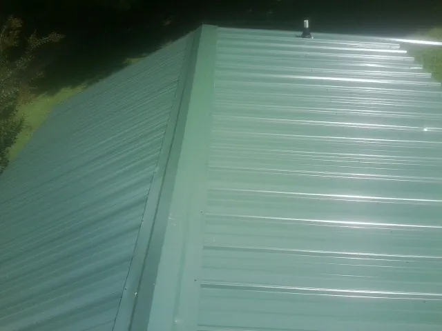 New green metal panels meeting at the ridge of a roof — Flat Roof Repair work by our crew in Twin Valley