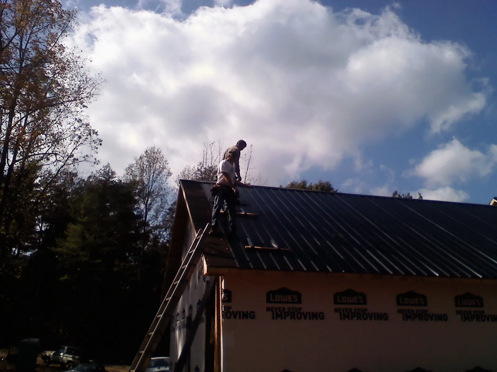 Roofer fastening dark metal panels high against a cloudy sky, from a Roof Inspection job in Twin Valley