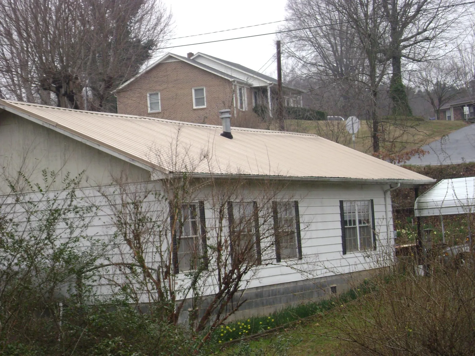 Tan metal roof on a white sided house set into a hillside — Commercial Roofing by Roofing Brothers in Twin Valley